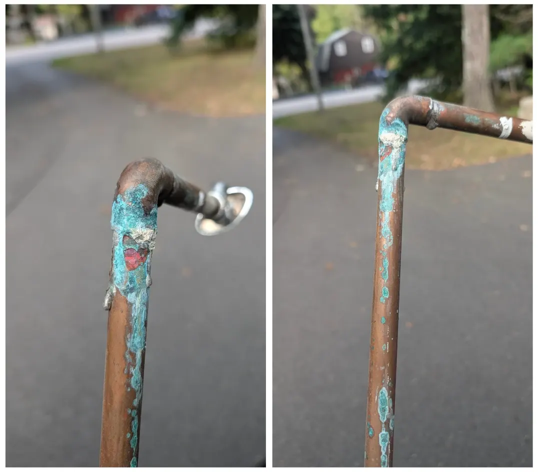 The photo shows severe green corrosion and mineral buildup along the copper pipe and fittings, with visible deterioration around the elbow and connection points**.
