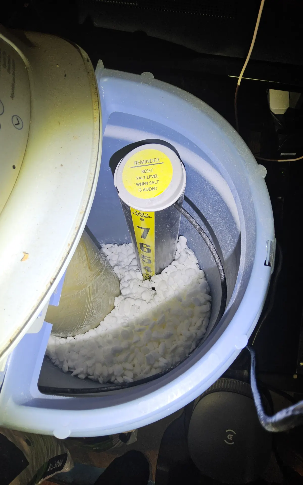 Close-up of a water softener brine tank showing the salt level indicator and white water softener salt pellets inside the tank.