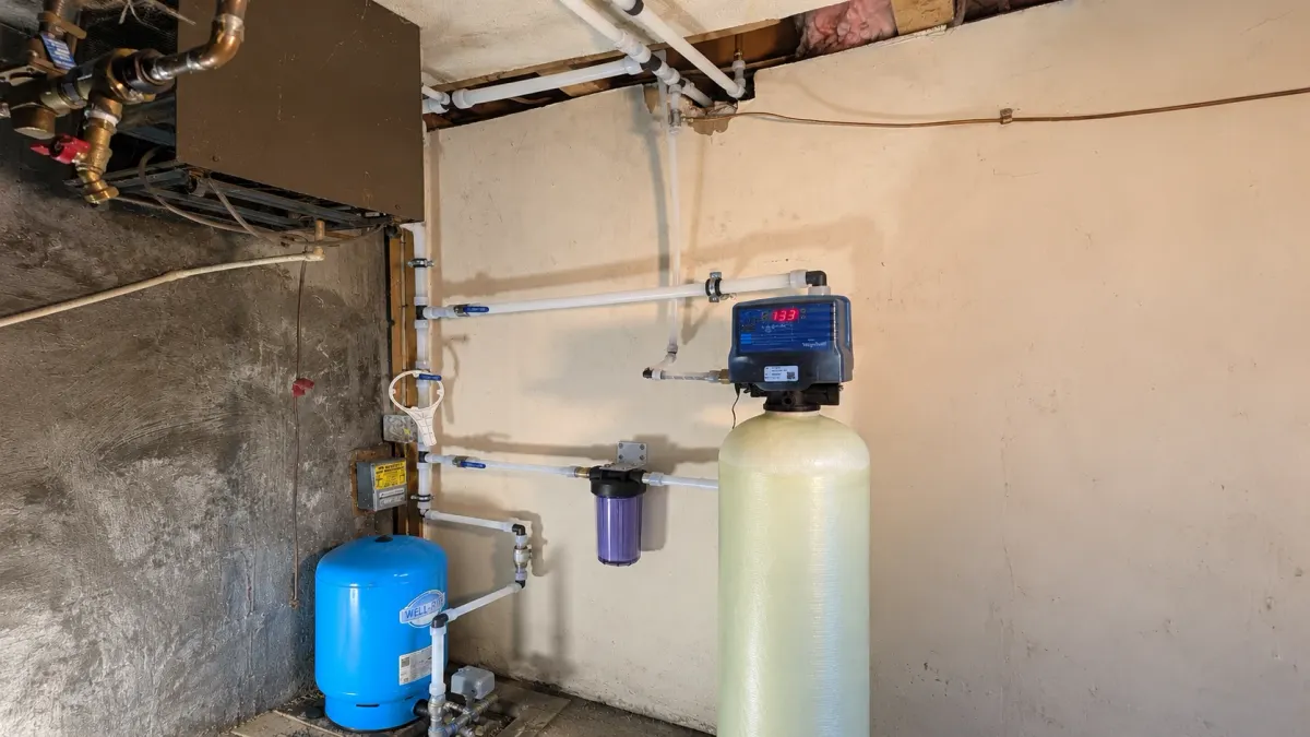 This photo shows a professionally installed whole-home water treatment system with a WaterSoft conditioning tank, filtration equipment, pressure tank, and connected water lines used to address well-water corrosion.